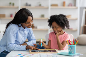 Woman sitting at desk with child who is writing on a blackboard